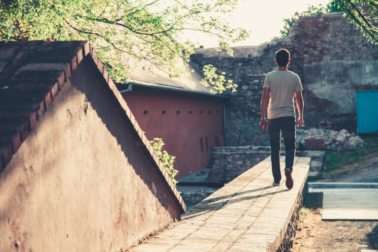 A man walks along a sunlit path in an urban setting, showcasing tranquility and solitude.