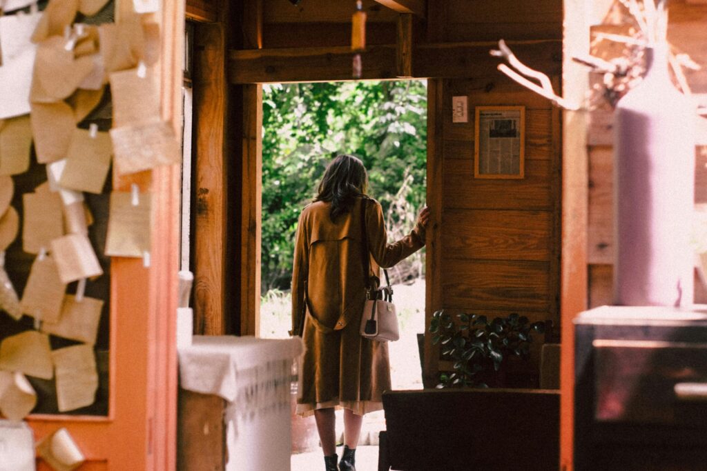 A woman in a warm coat steps out of a cozy cabin into the sunlight.