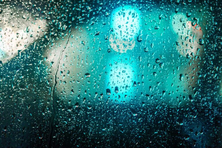 Raindrops on glass with blurred colorful lights creating a moody abstract background.