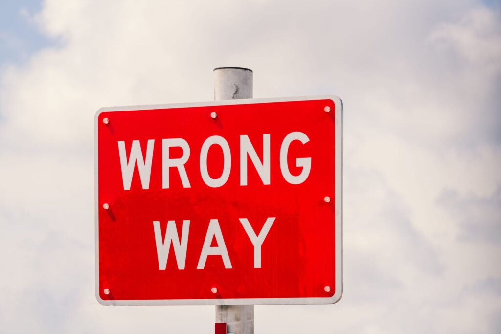Hiểu Bài Clear image of a bright red 'Wrong Way' traffic sign against a cloudy sky in Miami, Florida.